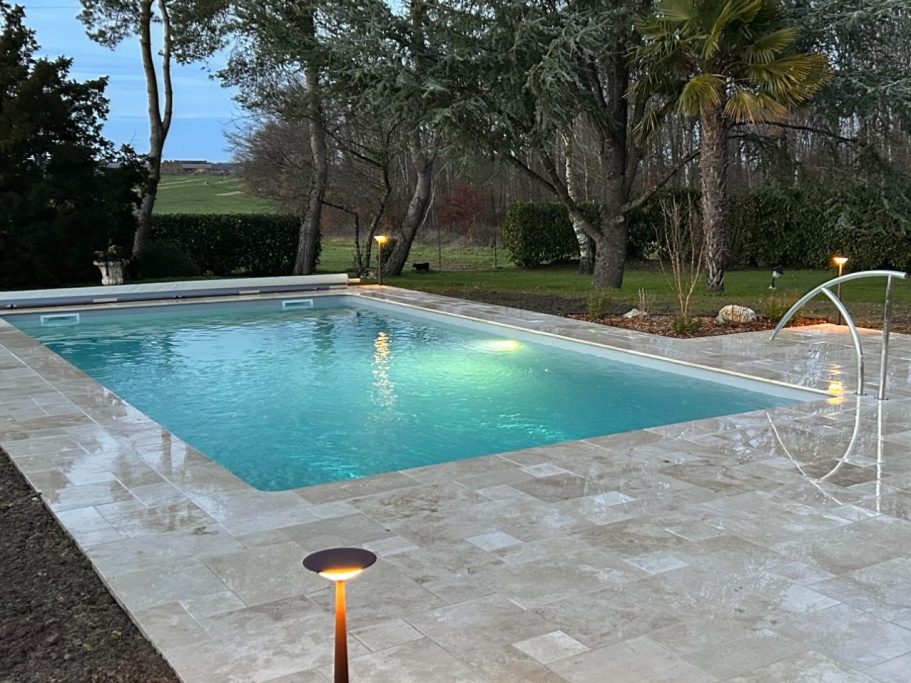 Piscine éclairée, entourée d'arbres et de lanternes, dans un jardin paisible.