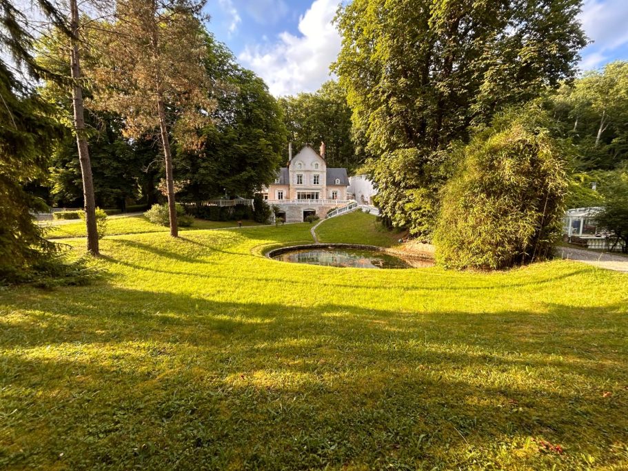 Maison blanche entourée d'arbres, avec un jardin verdoyant et un petit étang.
